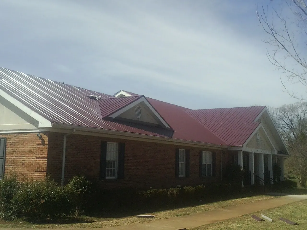 Red metal roof with gabled entries on a long brick building, from a Hail Damage Roof Repair job in Wrenshall