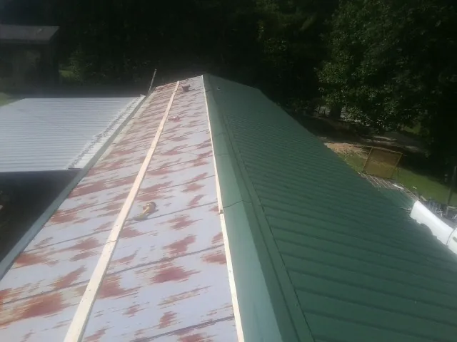 Old rusted panels beside newly installed green metal roofing — Wind Damage Roof Repair by Roofing Brothers in Wrenshall