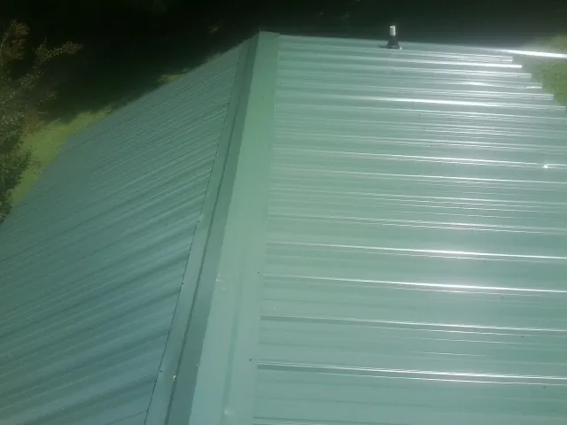 New green metal panels meeting at the ridge of a roof — Flat Roof Repair work by our crew in Wrenshall