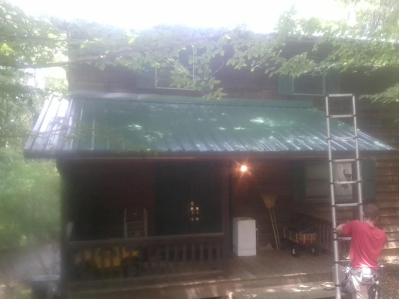 Worker on a ladder at the green porch roof of a wooded cabin in Wrenshall