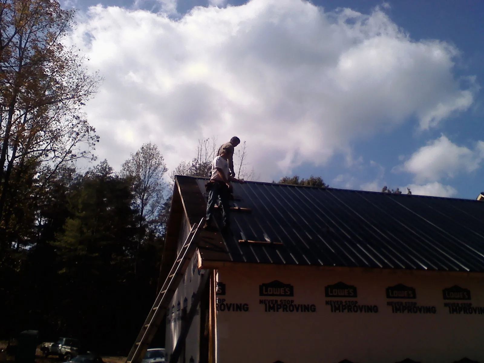 Roofer fastening dark metal panels high against a cloudy sky, from a Roof Inspection job in Wrenshall
