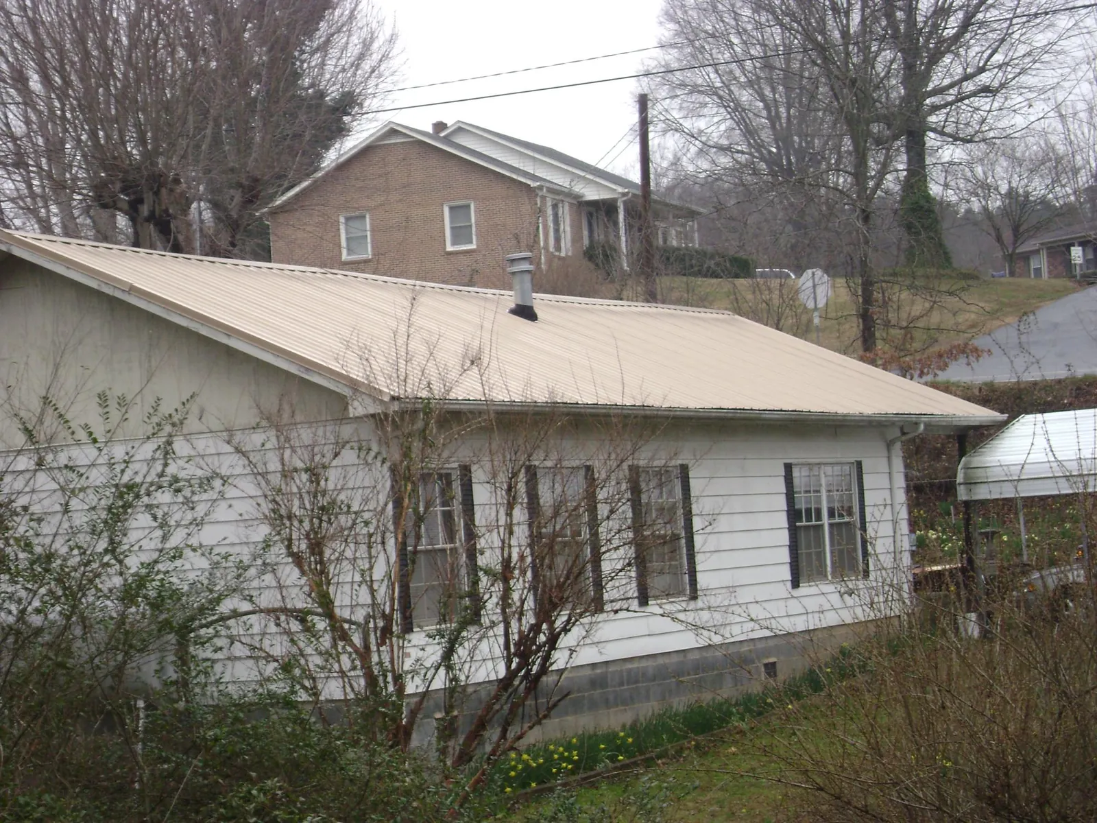 Tan metal roof on a white sided house set into a hillside — Commercial Roofing by Roofing Brothers in Wrenshall