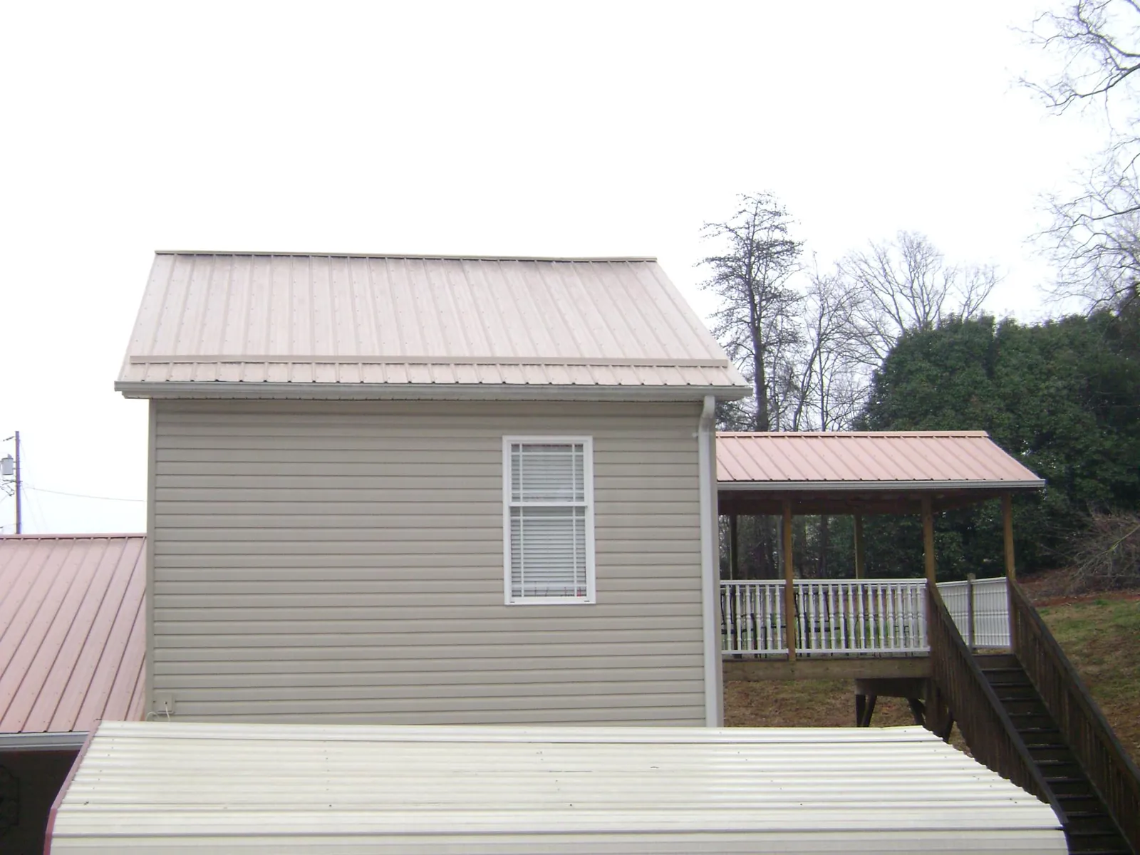Tan metal roofs on a two story addition and attached porch, from a Roof Replacement job in Wrenshall